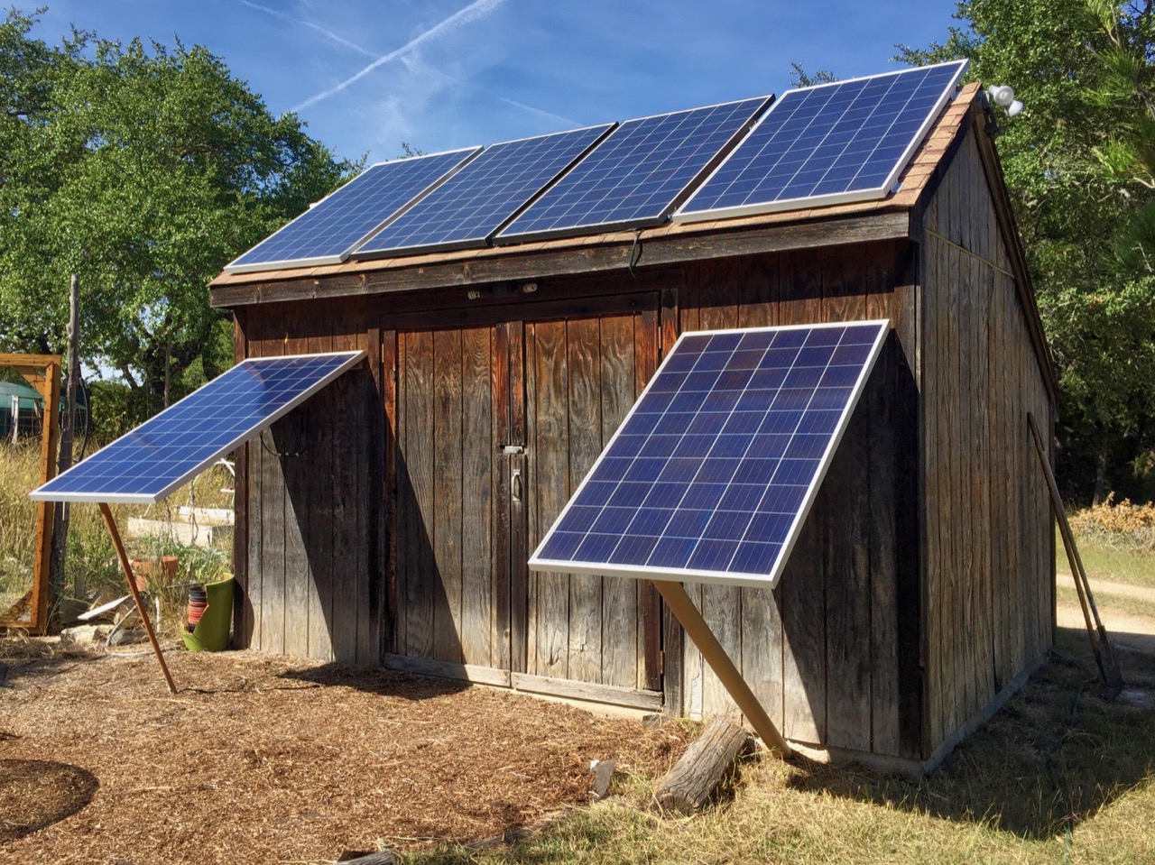 This meme is an image of a small, rustic wooden shed with solar panels on the roof. The panels are angled in a way that creates a humorous, exaggerated "face" with a "smile" made from the panels' reflective surfaces. The text "I can see you" is written in a playful, cursive font above the "smile", implying that the shed is "watching" or "judging" something.